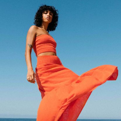 A woman wearing a matching red two-piece of summerwear from Billabong in front of a blue summer sky backdrop.