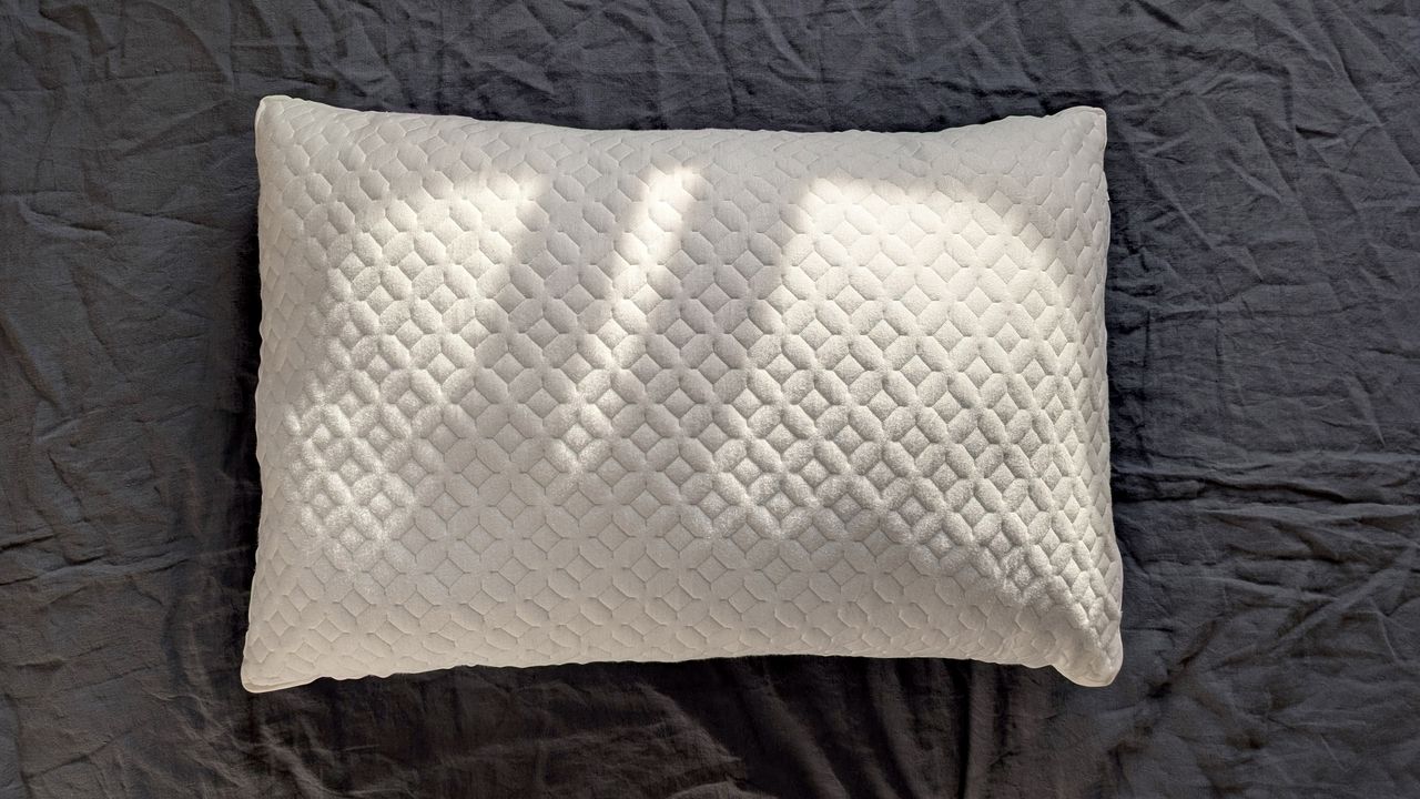 The Aeyla Adjustable FOAMO Pillow being tested on a bed with a grey linen duvet cover