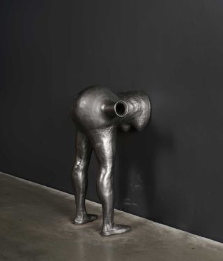 Sculpture of bent over grey human figure attached to wall