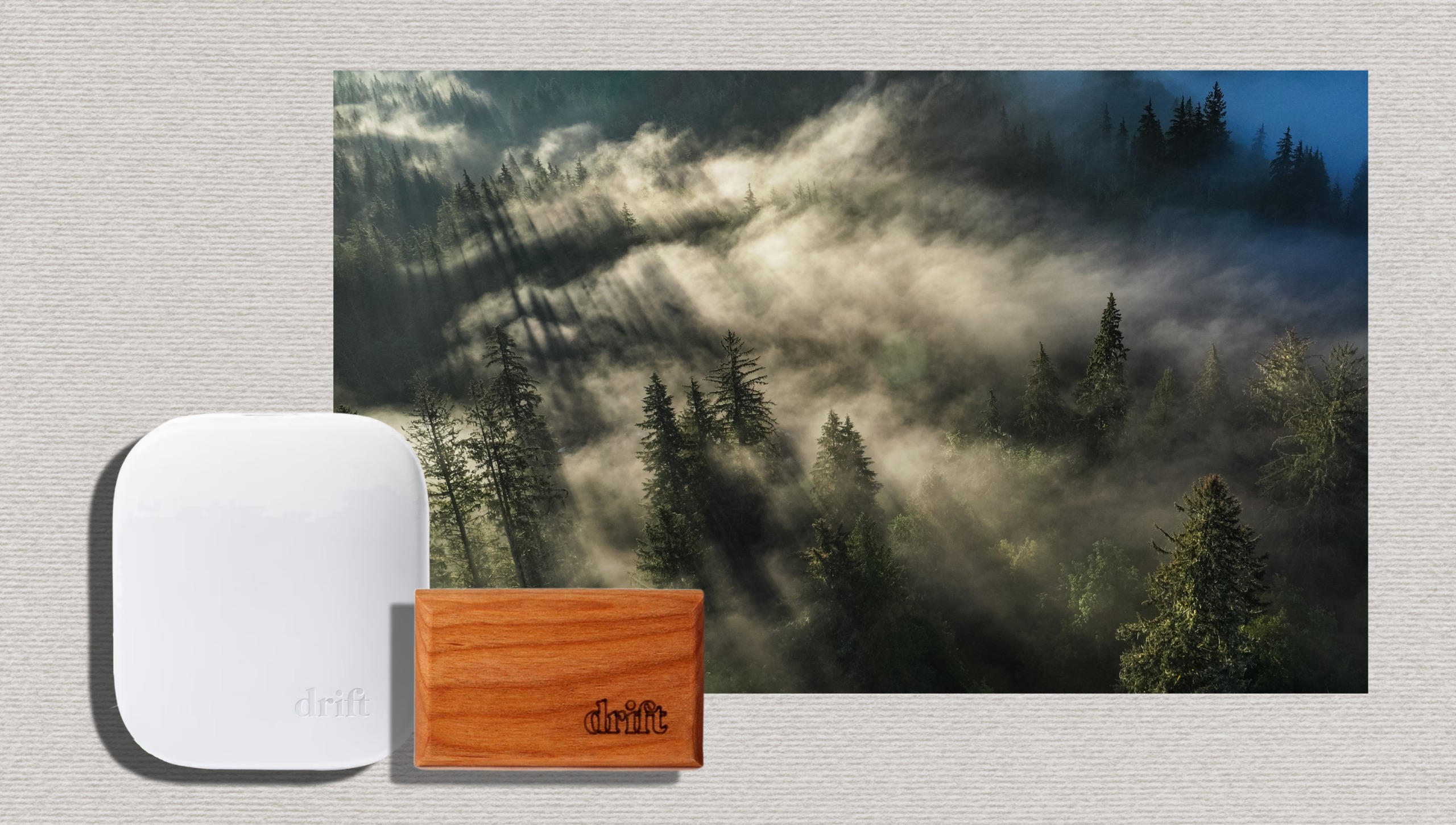 White Drift home diffuser and wooden car freshener beside a photo of a misty evergreen forest on a textured cream background