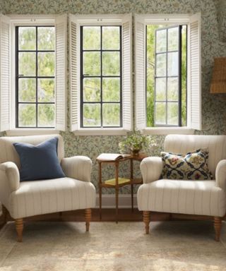 Two white chairs with cushions on next to three windows, with a rug underneath