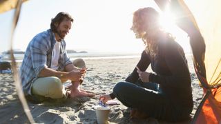 Woman and man playing cards outside tent on beach