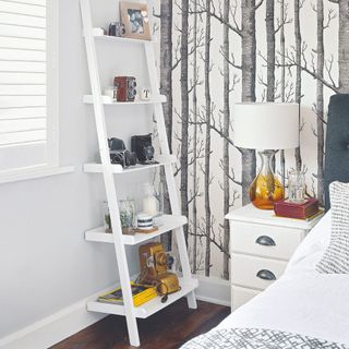 Bedroom with a ladder-style shelving, bedside table and tree-print wallpaper