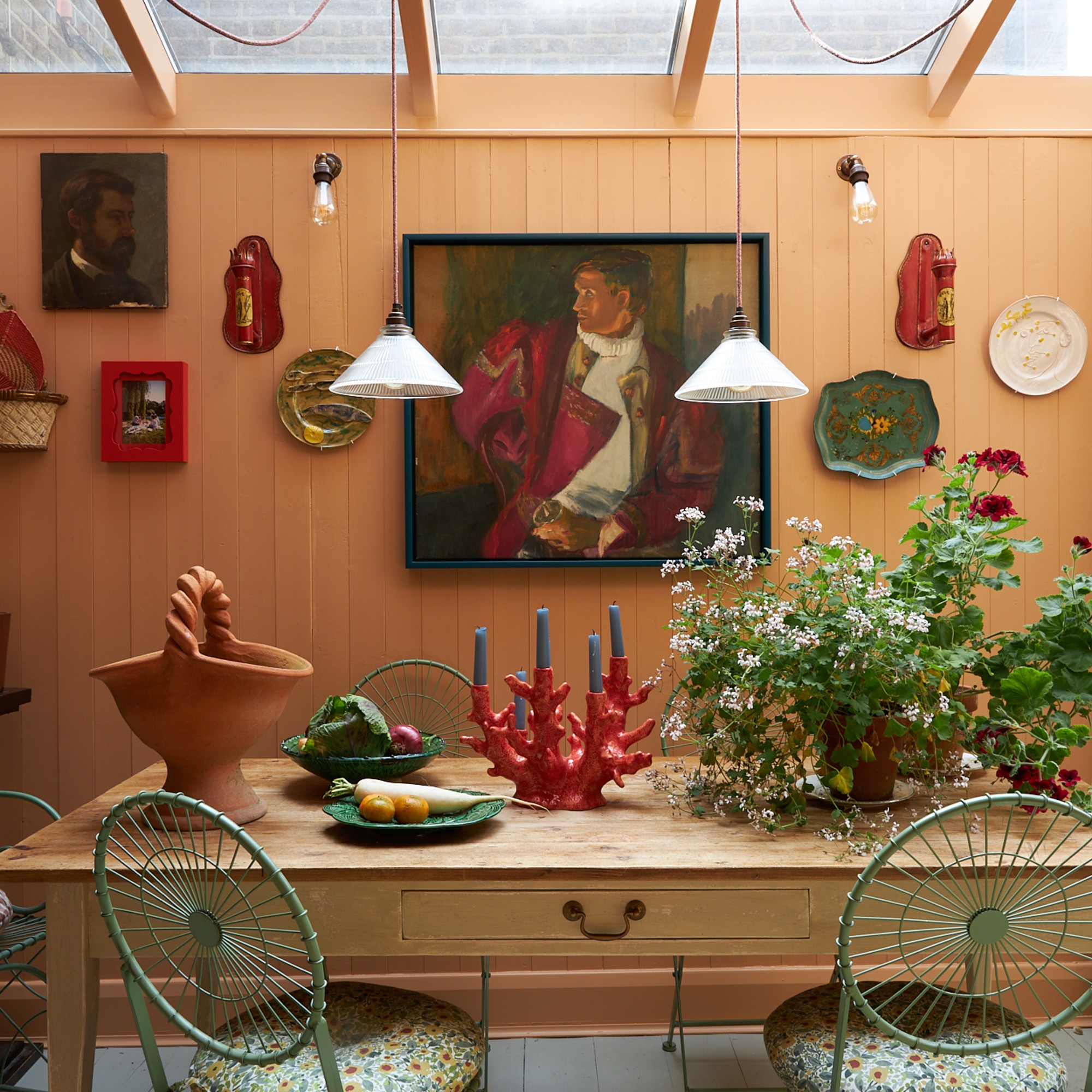 A panelled kitchen dining area painted in Farrow &amp; Ball's Fake Tan apricot shade with a rectangular wooden table and a gallery wall