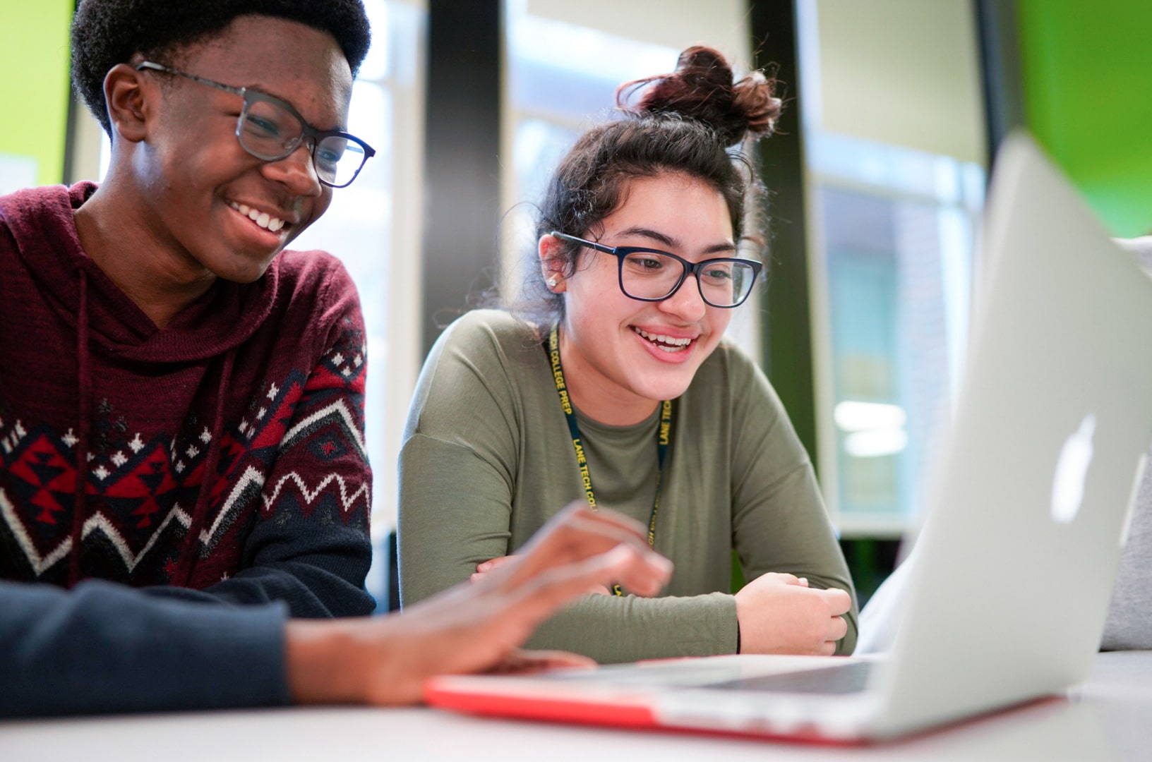 Two students sit in front of a MacBook laptop.