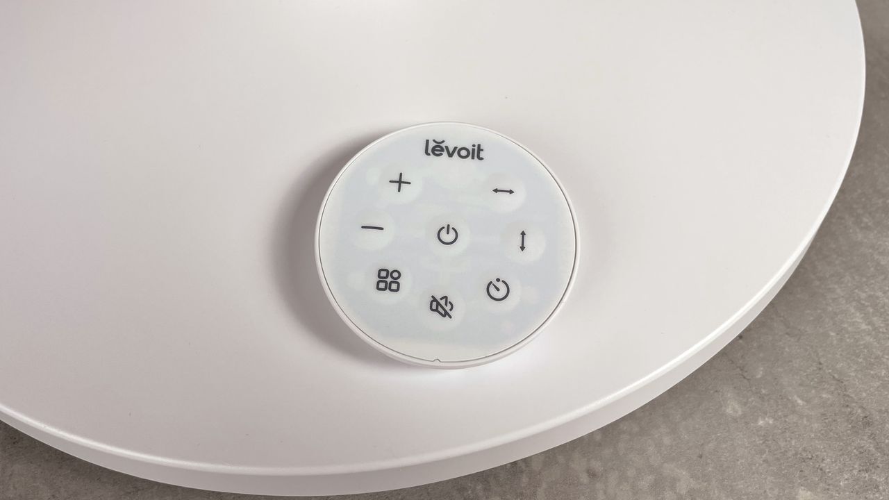 The round remote control is sitting on the base of the Levoit Pedestal Air Circulator Fan.
