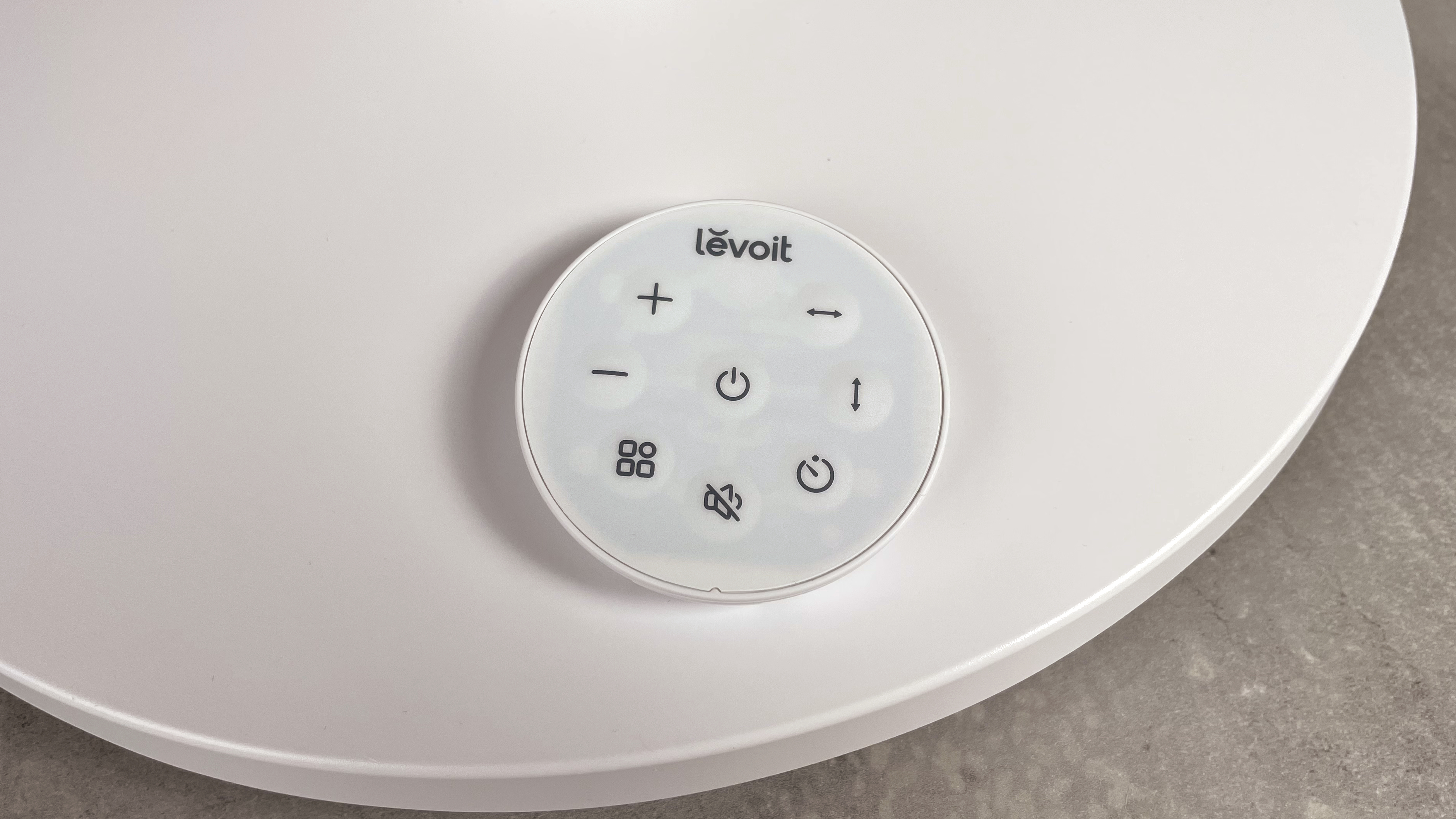The round remote control is sitting on the base of the Levoit Pedestal Air Circulator Fan.