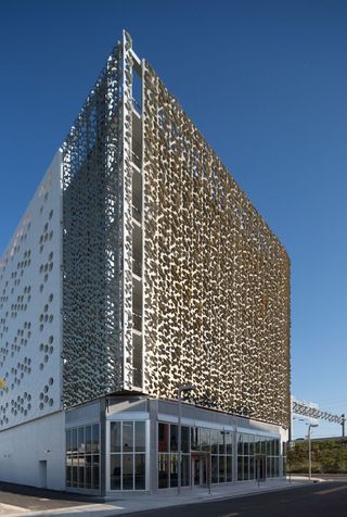 Daytime outside image of Leong Leong's elevation, building stands at 80 feet, white ground floor windows and doors, grass slope, street lights, road, pathway, blue sky