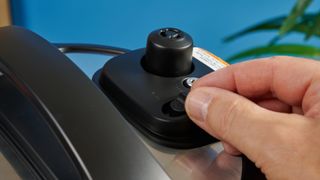 a black pressure cooker photographed against a blue background, showing its cooking presets, steam release valve, and Instant Pot branding