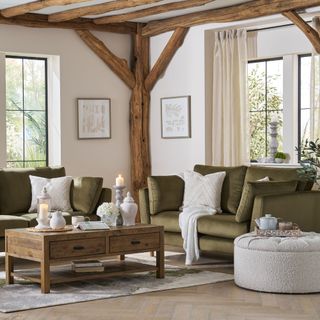 A living room with exposed beams and two olive green sofas and a patterned lighter rug with a wooden coffee table on top