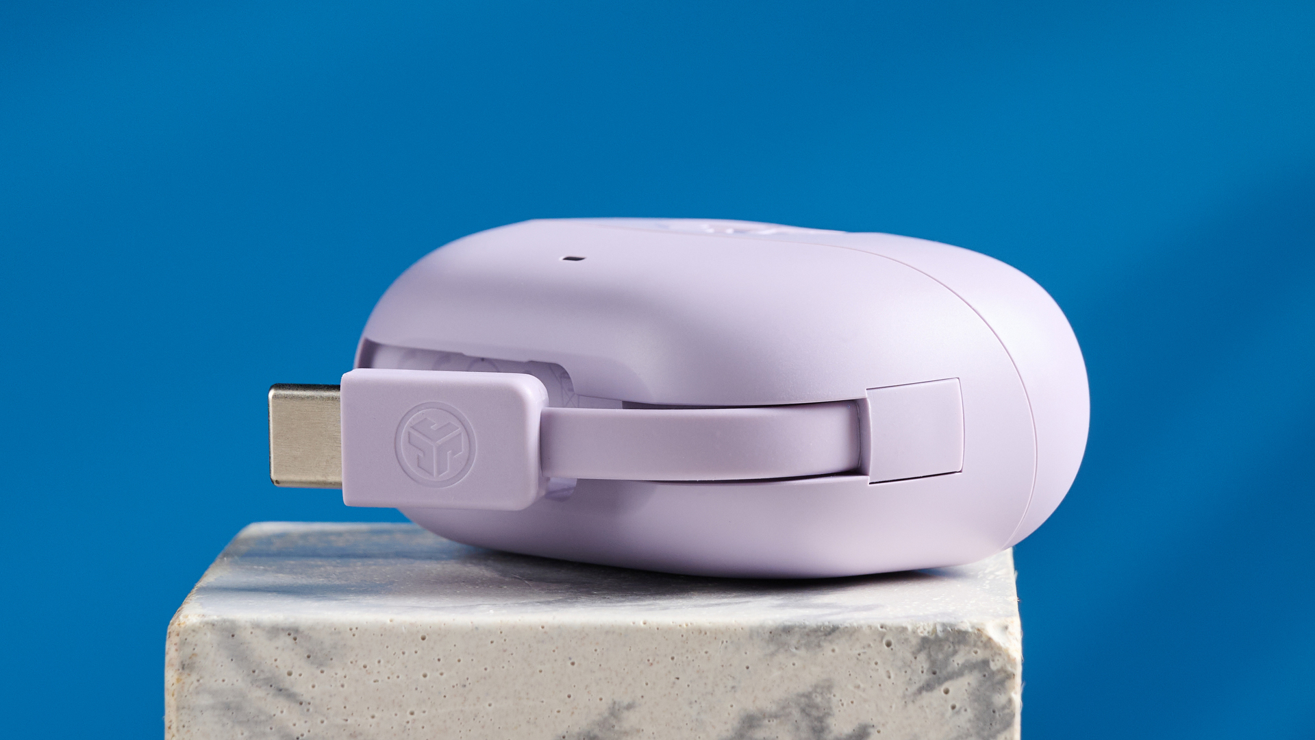 the jlab go pods anc earbuds in lilac with a lilac charging case and built in usb-c cable against a blue background on a marble stand