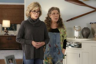 jane fonda and lily tomlin looking surprised and standing in a living room in the tv show grace and frankie