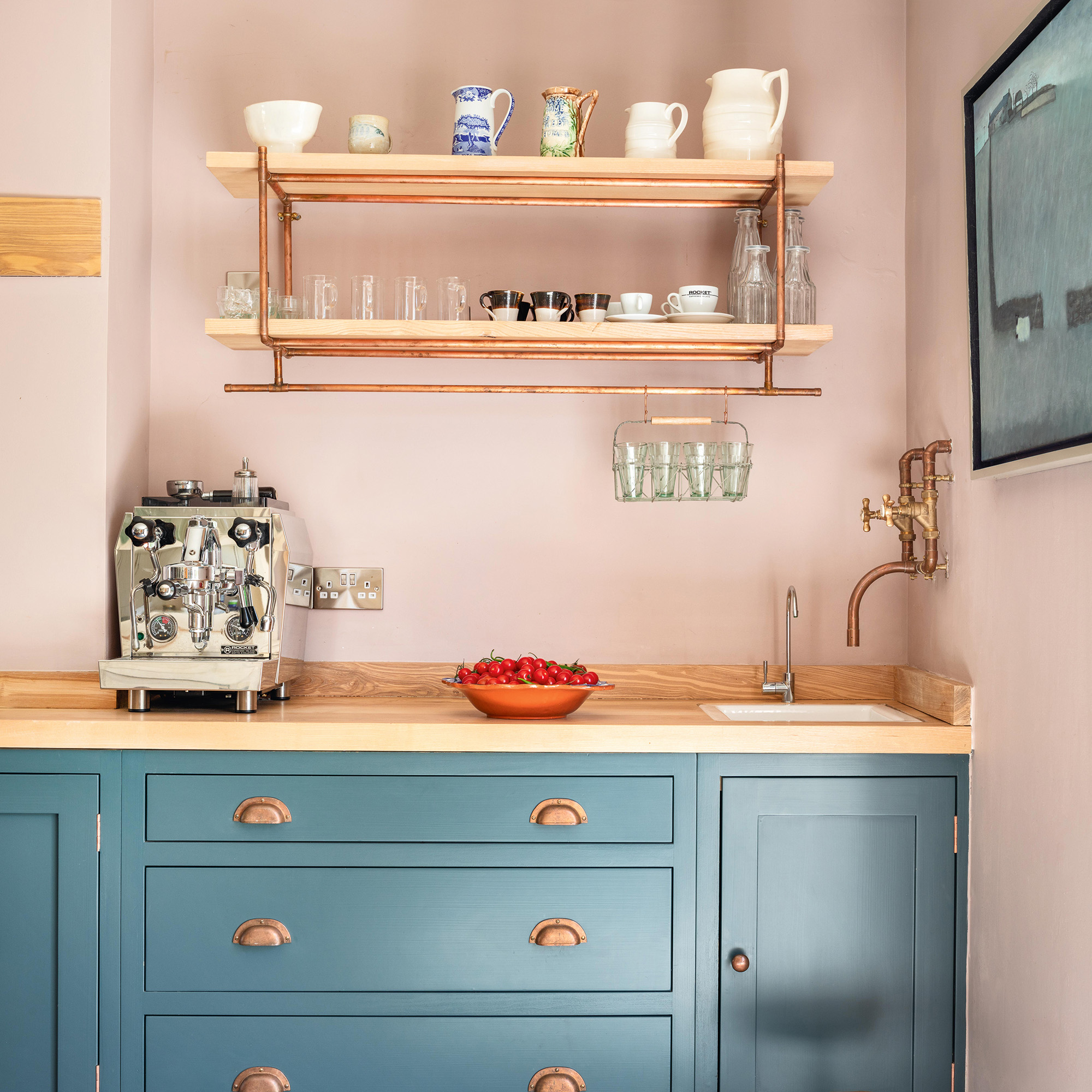 coffee station in country kitchen with pink walls and blue cabinetry and brass pipe open shelf with ash shelves and worktops