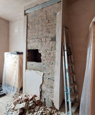 chimney breast with most of plaster removed, lintel in place and hole where bricks are being removed