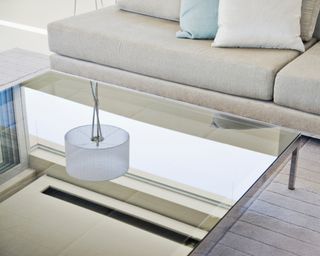 Glass coffee table reflecting image of ceiling lamp, with sofas nearby
