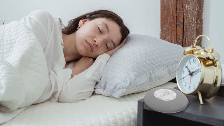 A woman sleeping with a white noise machine by her bed