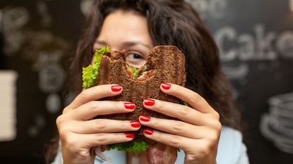 A woman peeks out from behind her sandwich.