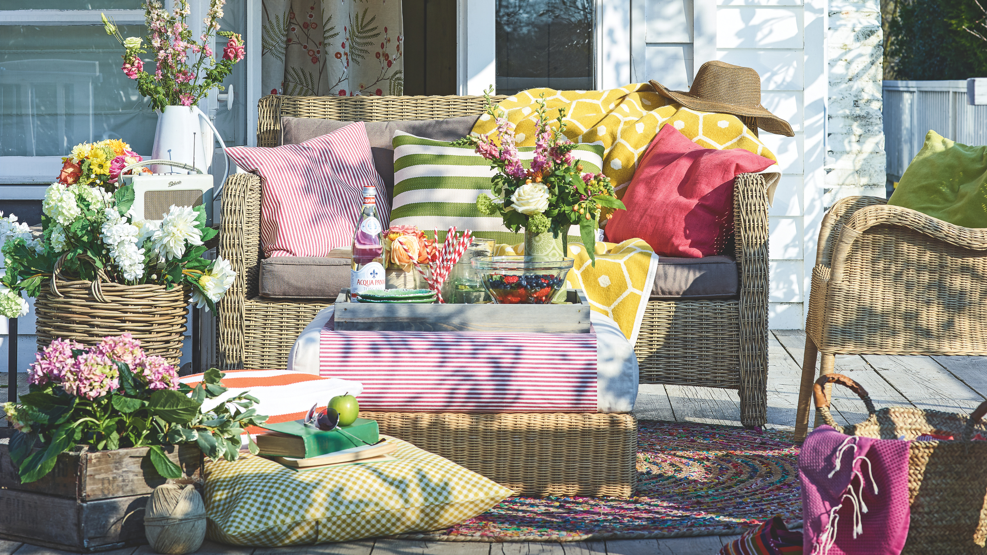 Rattan plant pot filled with whiteflowers, next to a rattan garden sofa, chair and coffee table.