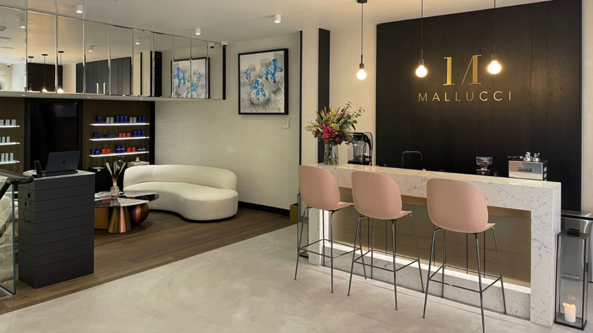 An image of Mallucci Mayfair clinic, with a marble bar and tall pink seats, a cream carpet, cream sofa and copper coffee table and shelves containing skincare products