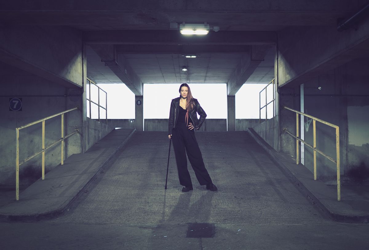 Portrait of a person with a cane standing in an industrial setting, taken on the OM System OM-3 with the OM System 25mm f/1.8 II lens
