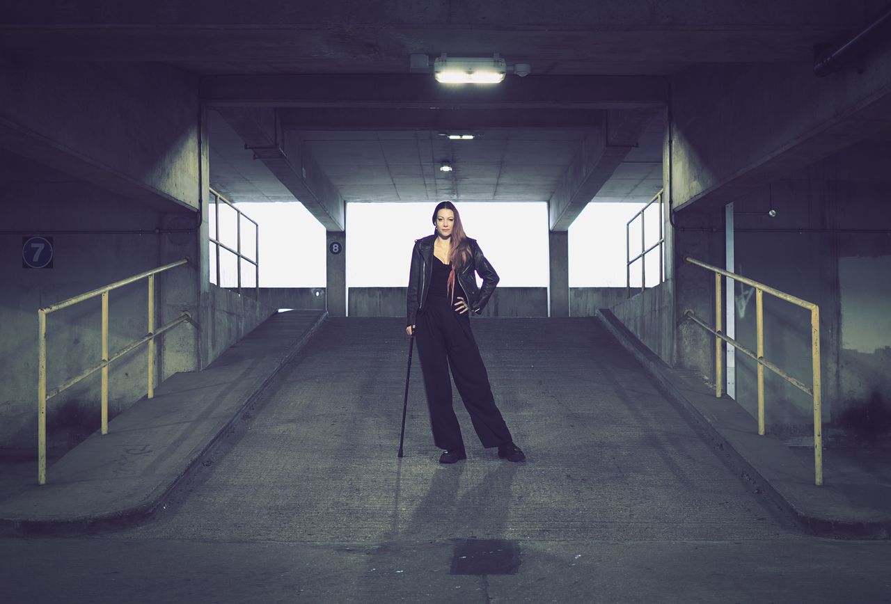 Portrait of a person with a cane standing in an industrial setting, taken on the OM System OM-3 with the OM System 25mm f/1.8 II lens