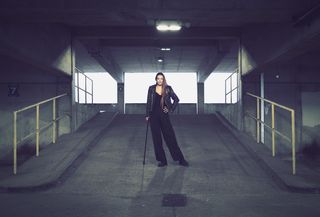 Portrait of a person with a cane standing in an industrial setting, taken on the OM System OM-3 with the OM System 25mm f/1.8 II lens