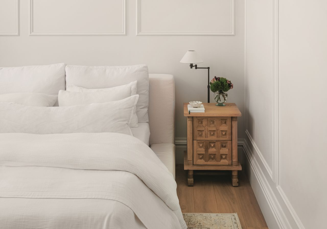 A neutral bedroom, a bed with white sheets, plump pillows, and a small wooden nightstand