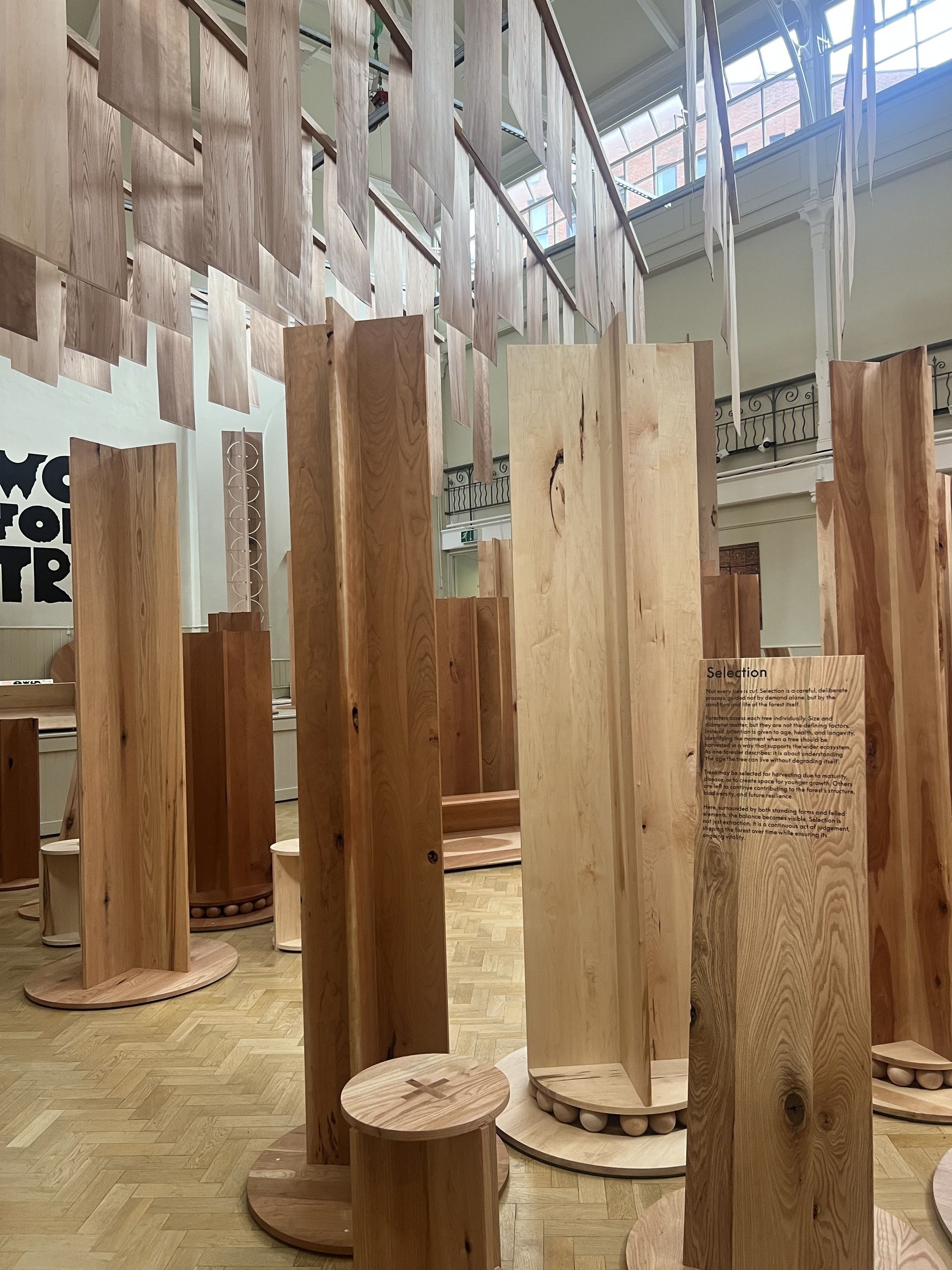 Image of an exhibition room with vertical wooden forms in various kinds of timber positioned around the space.