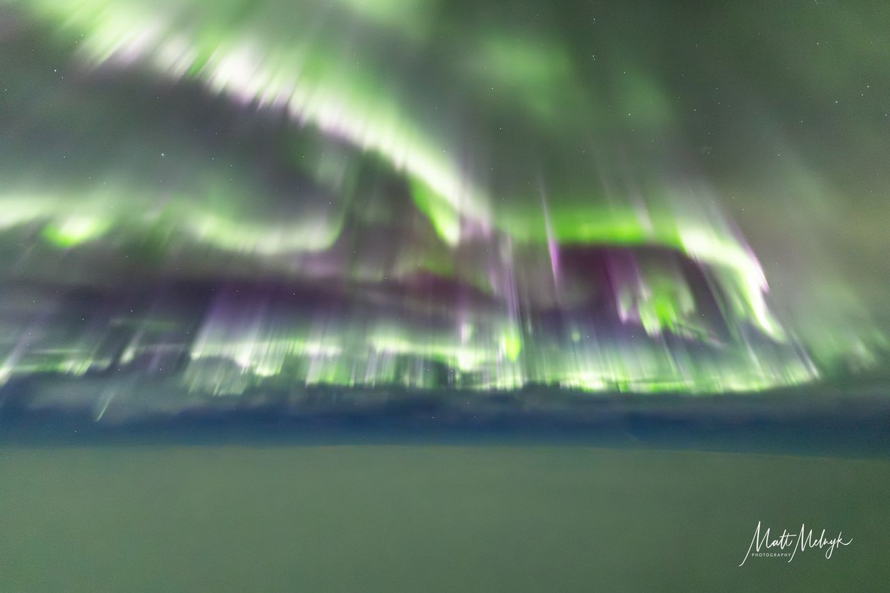 curtains of green auroras fill the sky, with a blanket of cloud below.