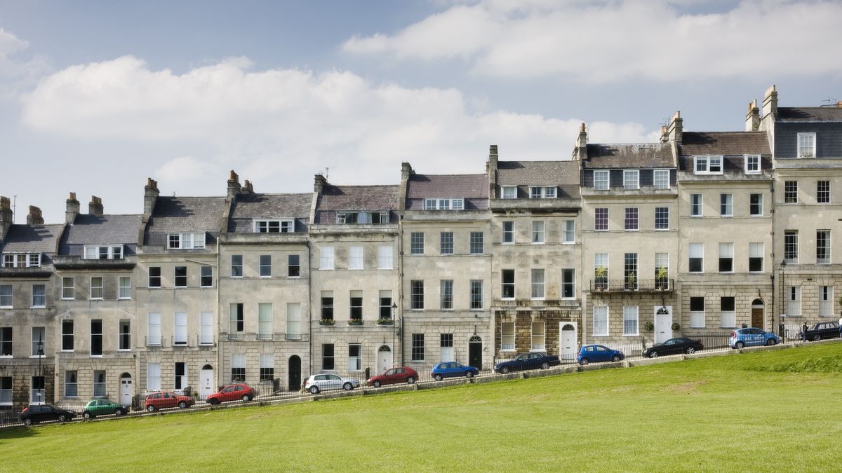 Terraced townhouses in the the Royal Crescent in Bath with cars parked in front and green