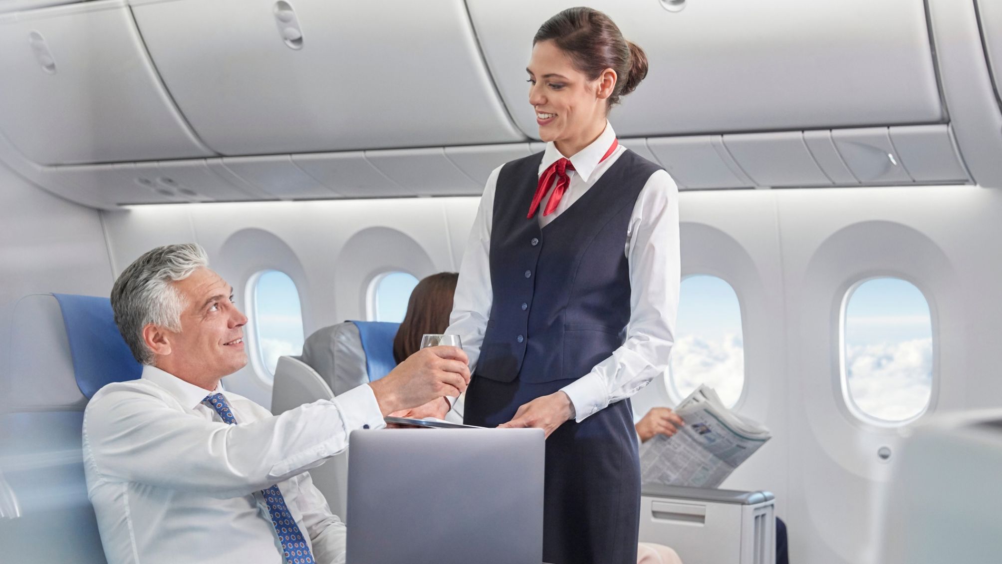 Flight attendant serving drink to businessman working at laptop on airplane