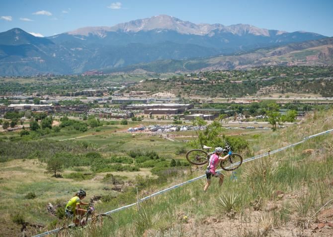 Riders from Stans No Tubes and Sports Garage make their way up a technical climb under the watchful of of Pike Peak in the background.