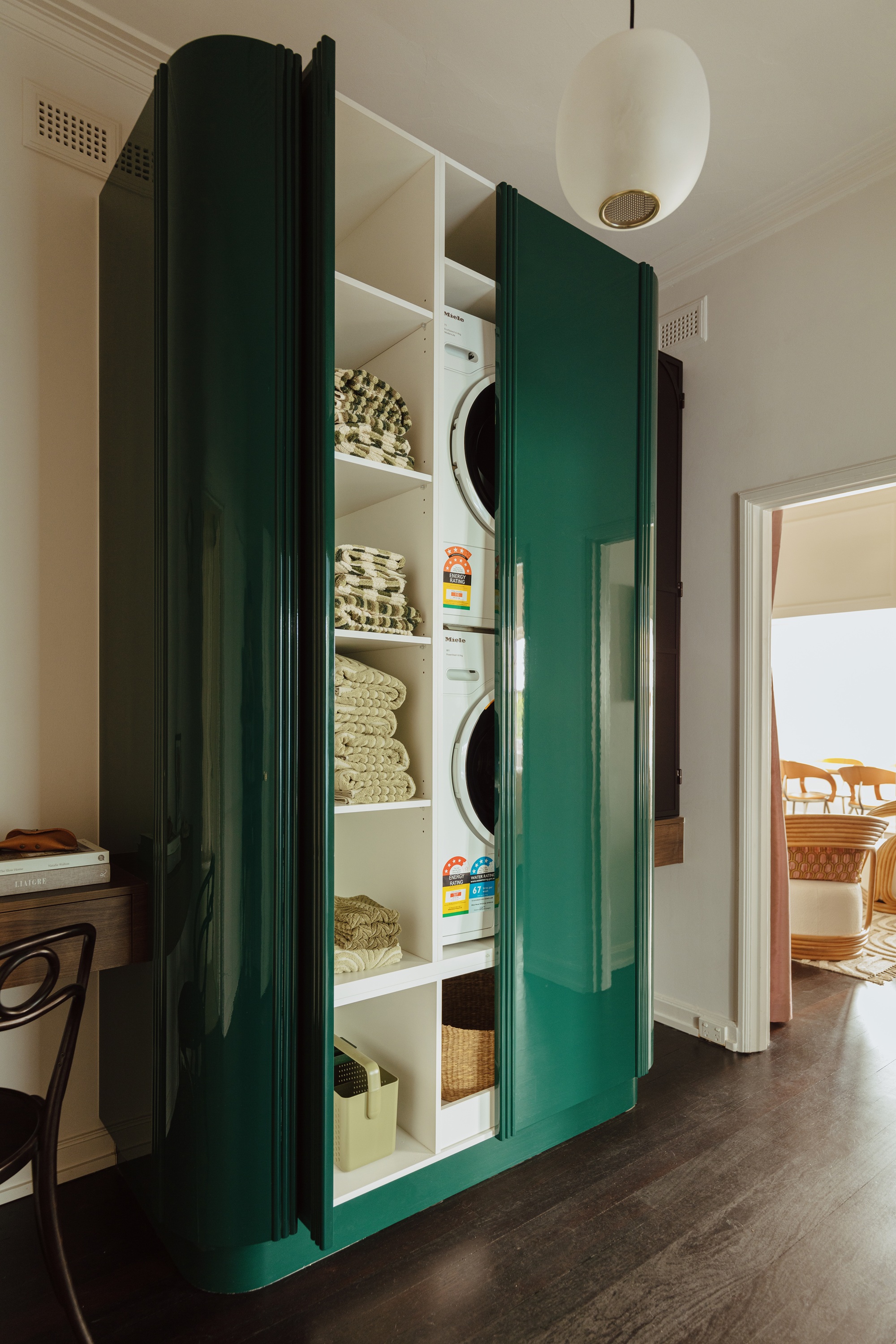 a laundry cabinet painted in a lacquered dark green with the door open so you can see a stacked washer and dryer inside.