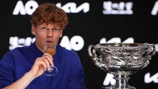Jannik Sinner sips from a glass of champagne, next to the Australian Open trophy, after winning the men's singles in 2025.