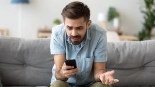 Man looking frustrated at his smartphone while sitting on a couch