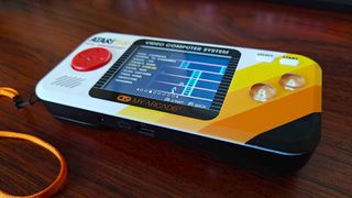 Atari Pocket Player Pro handheld on woodgrain desk with game menu on screen and "Fast Eddie" selected.