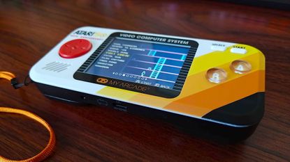 Atari Pocket Player Pro handheld on woodgrain desk with game menu on screen and "Fast Eddie" selected.