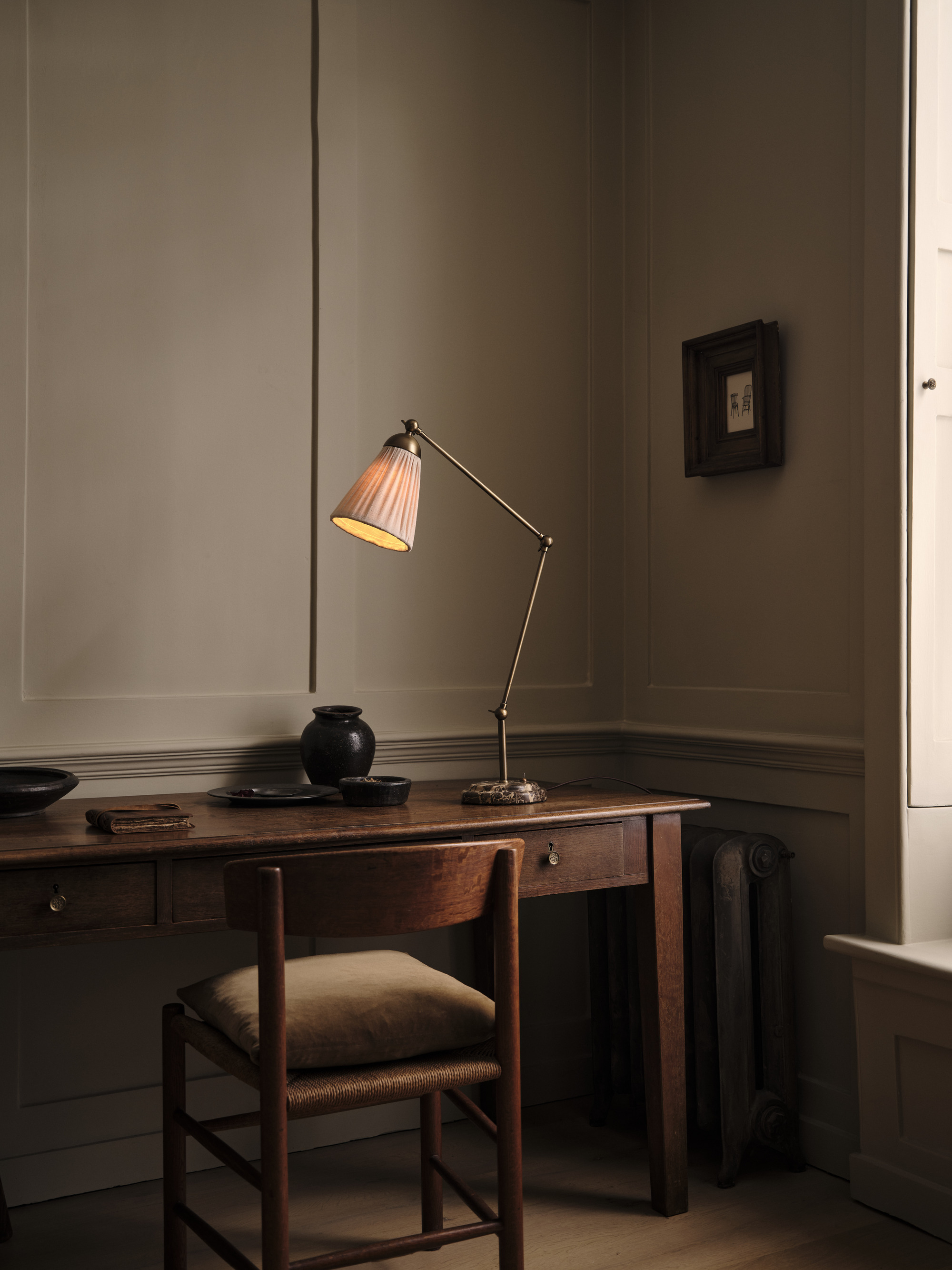 Image of a metal and fabric table lamp on an antique wood desk with a matching chair in a beige room.