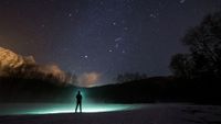 A person, with a glowing green outline, looking at the night sky with silhouetted hills.