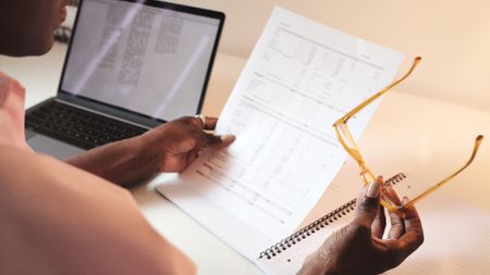 Woman sitting at a desk and looking at tax papers while holding her eyeglasses 