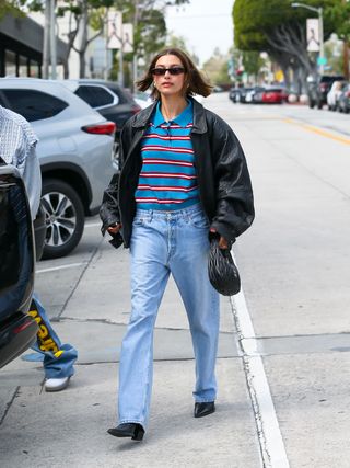 Hailey Bieber wears rugby shirt, jeans, and black leather jacket while walking around Los Angeles.