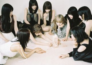 Twice sitting in a circle, from left: Jihyo, Dahyun, Nayeon, Momo, Sana, Tzuyu, Chaeyoung, Mina, Jeongyeon.