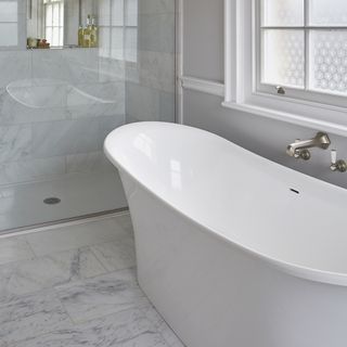 bathroom with large white bathtub near window with classic marble tiled flooring