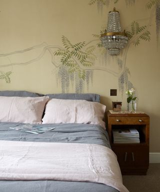 mural painted on a yellow bedroom wall with grey and pink bed linen