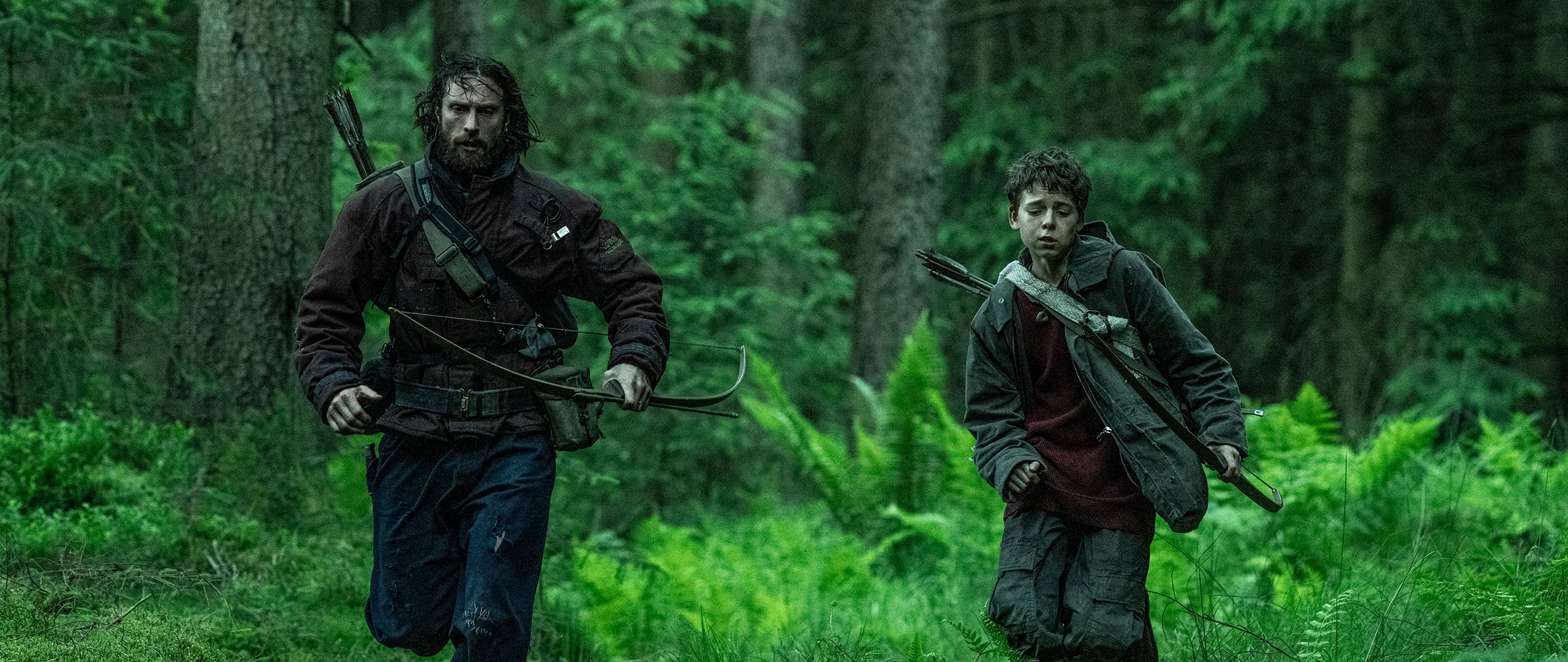 Aaron Taylor-Johnson and Alfie Williams run in a forest with bows on their back