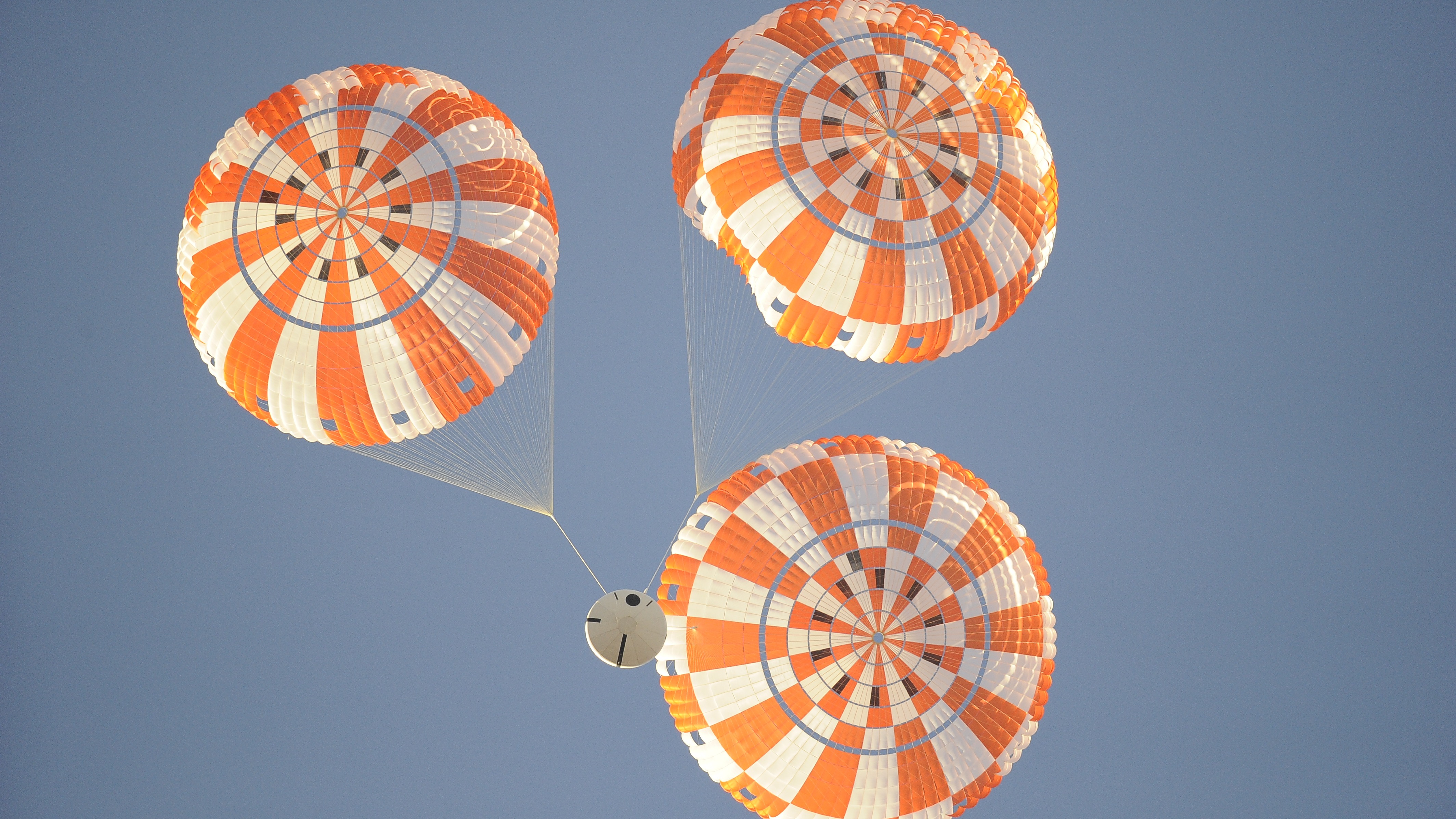 three orange parachutes above a spacecraft in mid-air