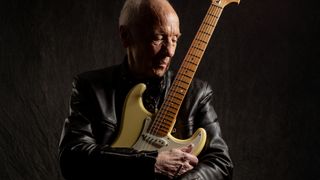 Robin Trower poses in a black leather jacket holding his signature yellow Fender Stratocaster