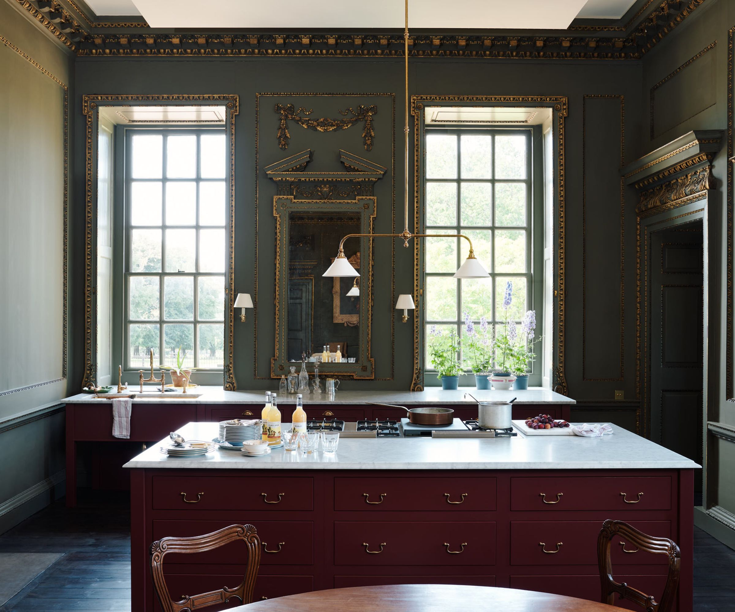 A stately home kitchen with green walls, red cabinetry, and marble countertops