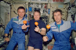 The Expedition 1 crew members are about to eat fresh fruit in the form of oranges onboard the Zvezda Service Module of the Earth-orbiting International Space Station (ISS). Pictured, from the left, are cosmonaut Yuri P. Gidzenko, Soyuz commander; astronaut William M. Shepherd, mission commander; and cosmonaut Sergei K. Krikalev, flight engineer.