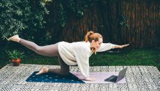 Woman doing Reformer Pilates at home on yoga mat in garden